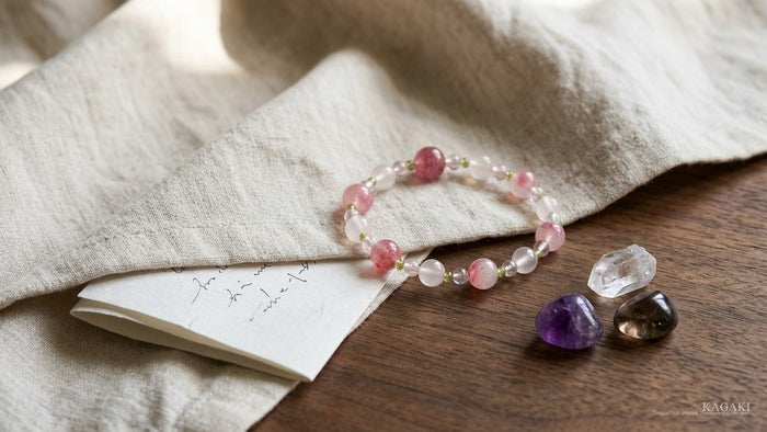 KAGAKI Spring handmade rose quartz and strawberry quartz beaded bracelet shown with starter amethyst, clear quartz and smoky quartz tumbled stones on cream linen — a beginner-friendly editorial image for a guide to crystals for beginners.