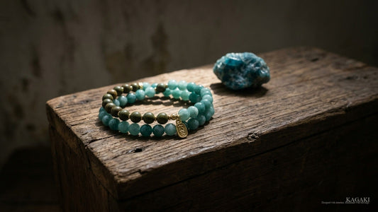 KAGAKI Forest handmade blue apatite and sandalwood bracelet at rest on aged walnut beside a small raw blue apatite stone in soft afternoon daylight, shown as an editorial hero image for a guide on choosing a handmade spiritual bracelet.