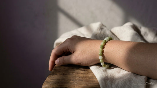 KAGAKI Meadow natural green jade beaded bracelet at rest on a partial wrist in soft afternoon daylight, shown as an editorial atmospheric hero image for an essay on jade color and meaning.