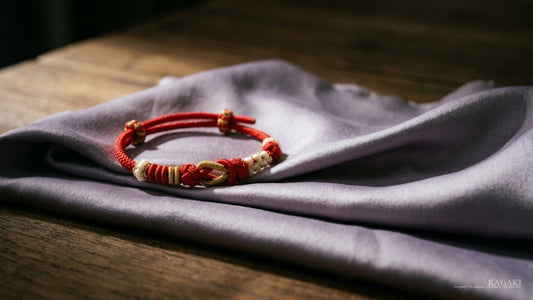KAGAKI Tether handmade Tibetan red string couple bracelet at rest on softly folded dusty-lavender silk in soft afternoon daylight, shown as an editorial hero image for a guide on spiritual gifts for women.