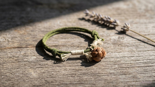 KAGAKI Lotus handmade Tibetan cord meditation bracelet at rest on aged walnut beside a single dried botanical sprig in soft afternoon daylight, shown as an editorial hero image for a guide on what a meditation bracelet is used for.