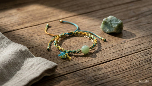 KAGAKI Loom handmade double-layer jade cord bracelet at gentle rest on aged walnut beside a small raw natural jade stone and folded cream linen in soft afternoon daylight, shown as a editorial hero image for a complete guide to jade.