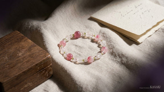 KAGAKI Spring handmade rose quartz bracelet at rest on softly folded cream linen beside a folded handwritten note and a small worn wooden box in soft afternoon daylight, shown as an editorial hero image for an essay on why small objects matter.