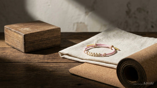 KAGAKI Japanese Zen Sakura handmade cord bracelet at rest beside a folded cream linen and partially rolled yoga mat in soft afternoon daylight, shown as an editorial hero image for a guide on yoga gifts.