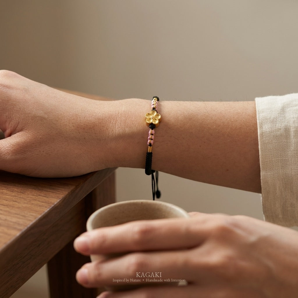 KAGAKI handmade cord bracelet sakura plum blossom cord bracelet (ink & petal) — black / green / red with gold accent, wrist wearing image.