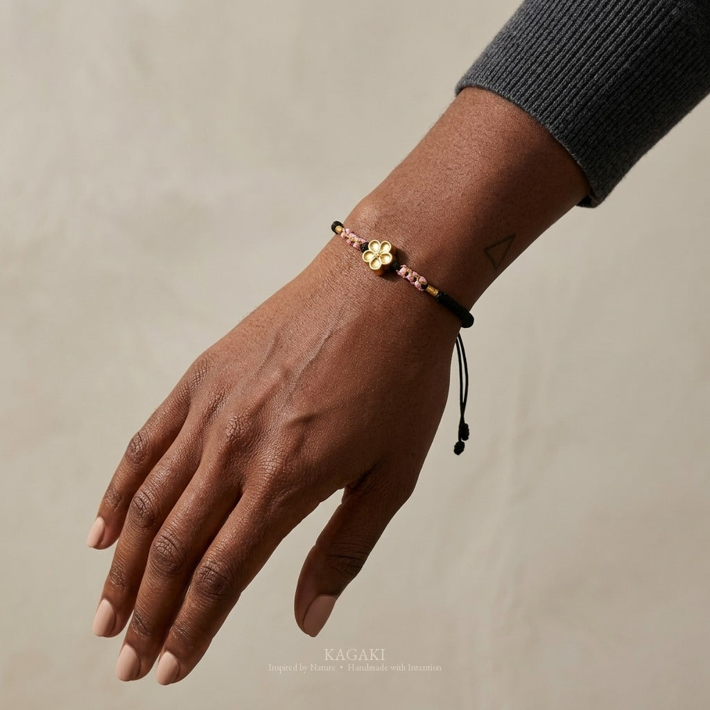KAGAKI handmade cord bracelet sakura plum blossom cord bracelet (ink & petal) — black / green / red with gold accent, luxury jewelry editorial wearing shot.