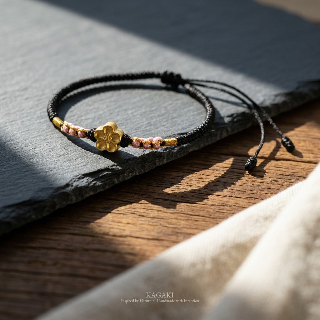 KAGAKI handmade cord bracelet sakura plum blossom cord bracelet (ink & petal) — black / green / red with gold accent, editorial styled scene.