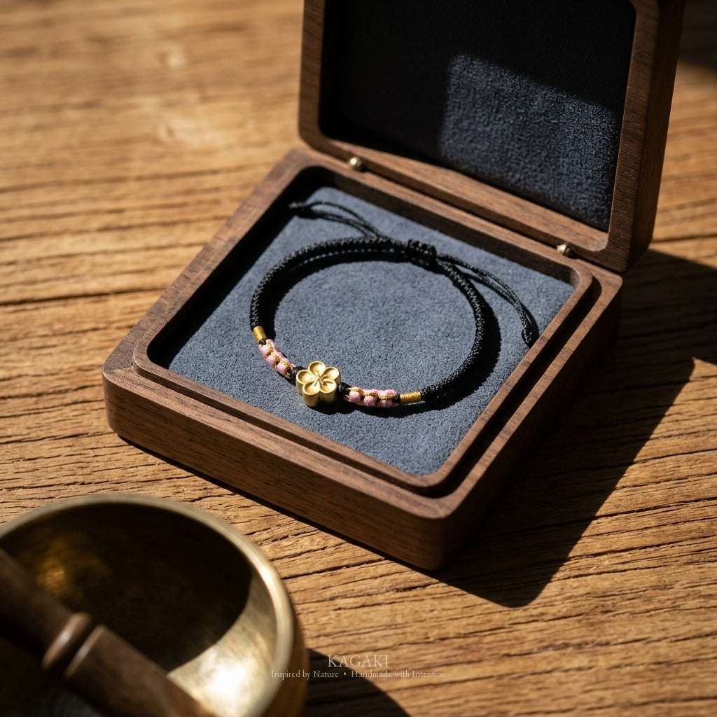 KAGAKI handmade cord bracelet sakura plum blossom cord bracelet (ink & petal) — black / green / red with gold accent, editorial styled scene.