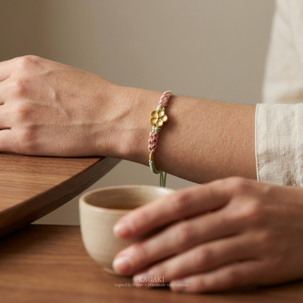 KAGAKI handmade cord bracelet sakura plum blossom cord bracelet (moss & petal) — black / green / red with gold accent, wrist wearing image.