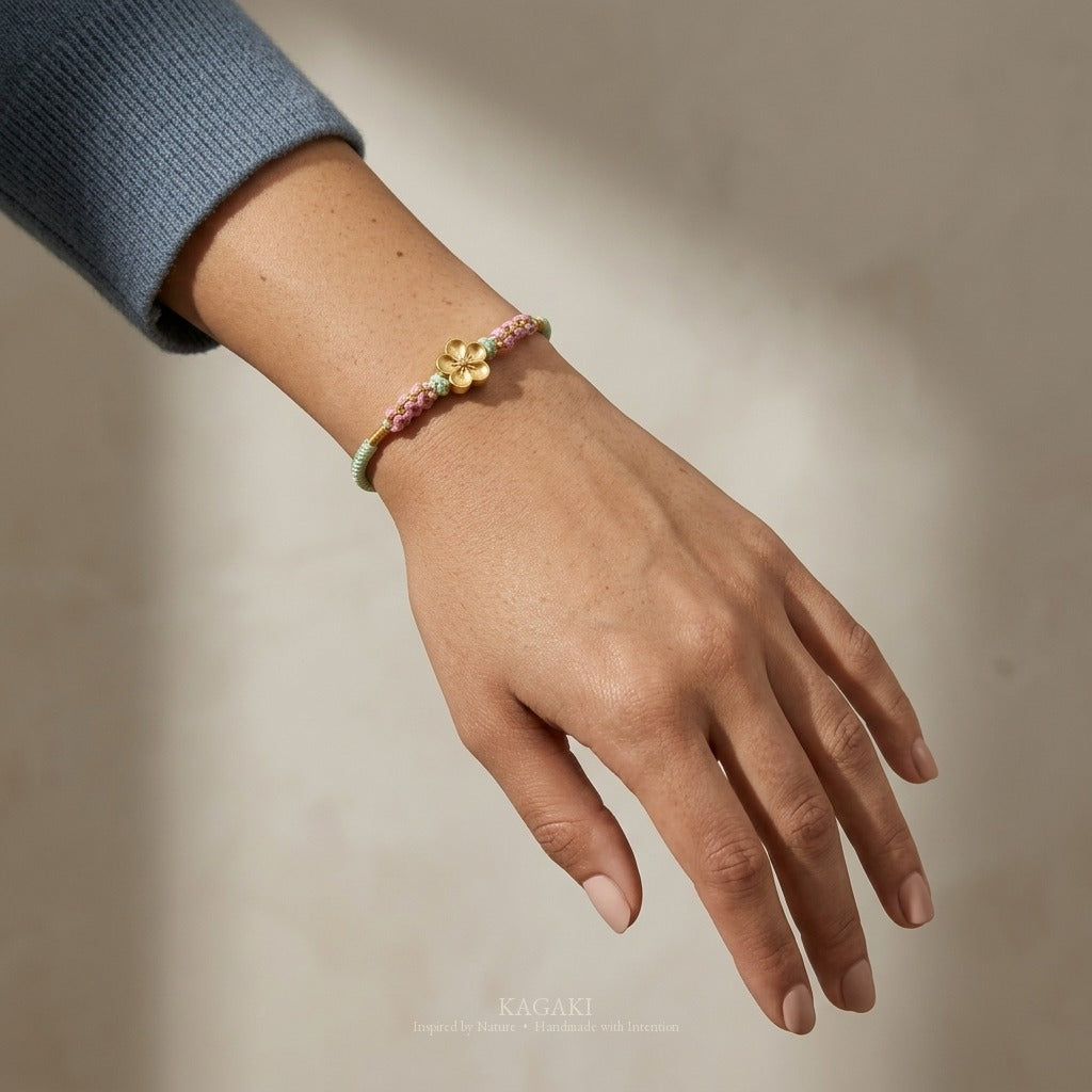 KAGAKI handmade cord bracelet sakura plum blossom cord bracelet (moss & petal) — black / green / red with gold accent, luxury jewelry editorial wearing shot.