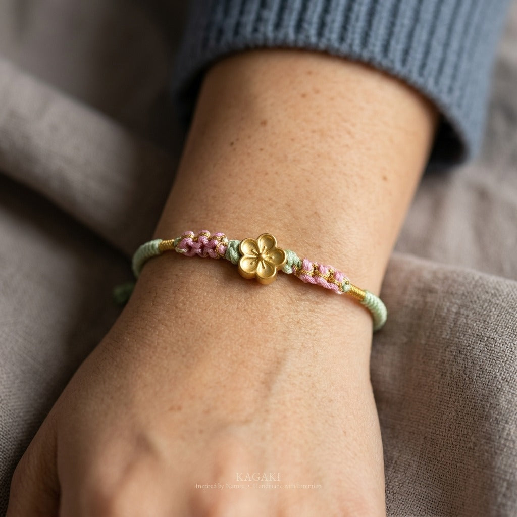 KAGAKI handmade cord bracelet sakura plum blossom cord bracelet (moss & petal) — black / green / red with gold accent, natural lifestyle wrist detail.