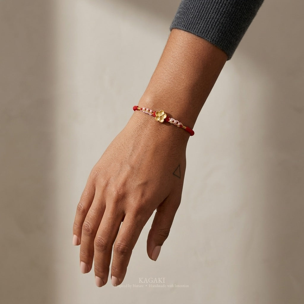 KAGAKI handmade cord bracelet sakura plum blossom cord bracelet (vermilion & petal) — black / green / red with gold accent, luxury jewelry editorial wearing shot.