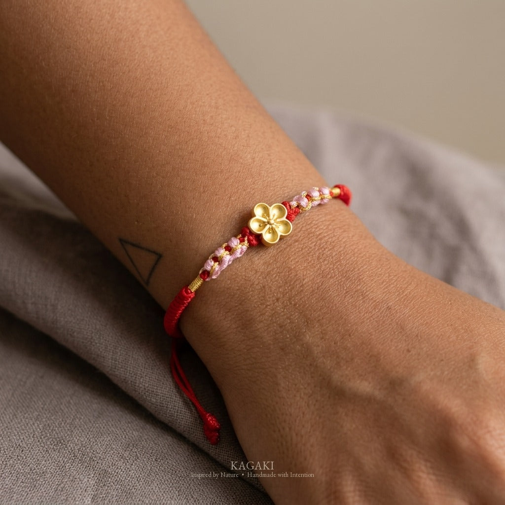 KAGAKI handmade cord bracelet sakura plum blossom cord bracelet (vermilion & petal) — black / green / red with gold accent, natural lifestyle wrist detail.