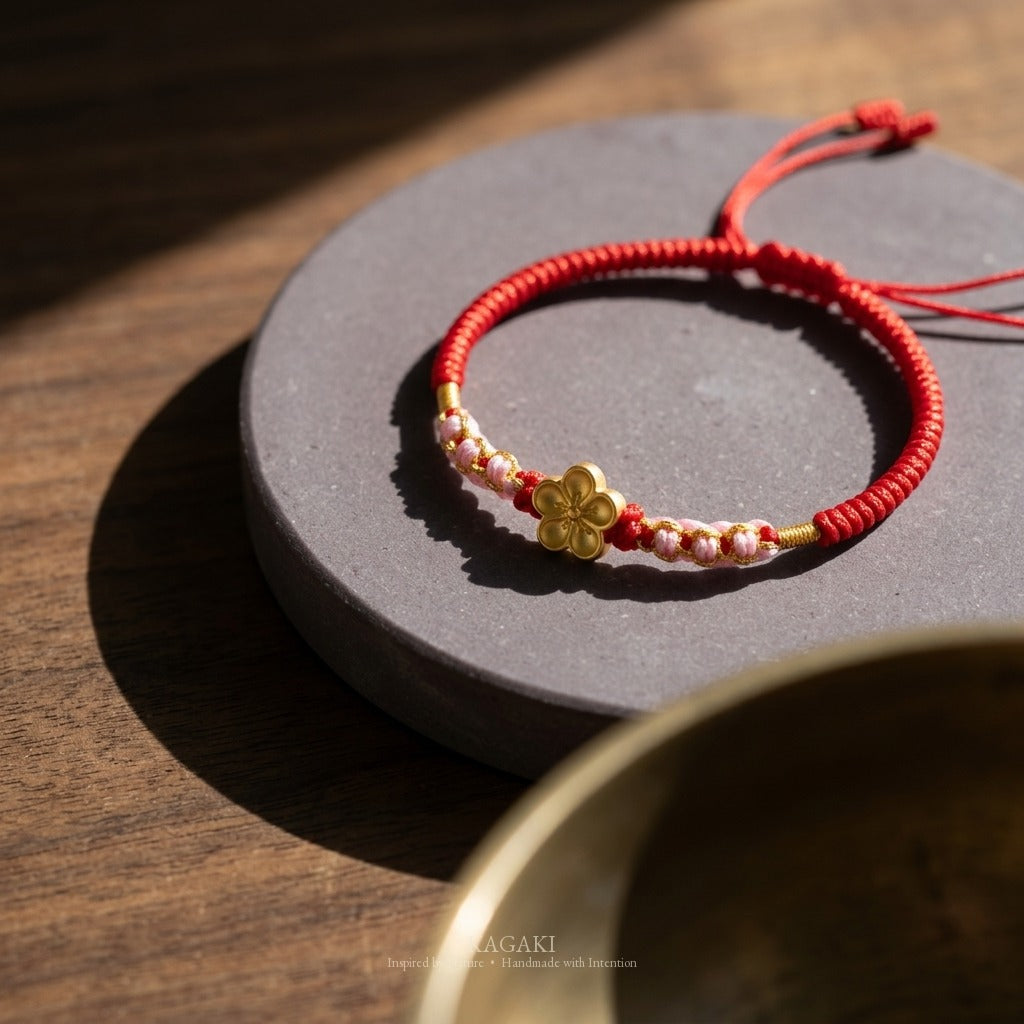 KAGAKI handmade cord bracelet sakura plum blossom cord bracelet (vermilion & petal) — black / green / red with gold accent, editorial styled scene.