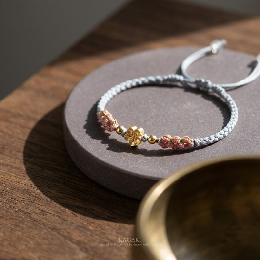 KAGAKI handmade cord bracelet sakura pastel cord bracelet (mist & petal) — mist blue or dawn pink with gold accent, editorial styled scene.