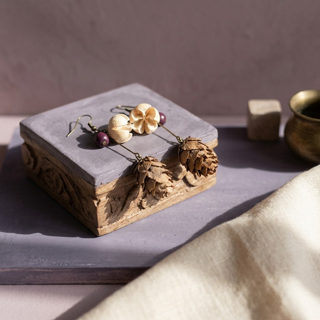 KAGAKI dried-botanical earrings displayed on a hand-carved wood pedestal with dusty violet plaster — a multi-plane meditation altar still-life.