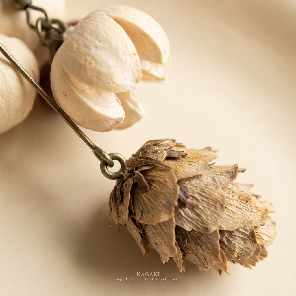 Macro close-up of the cream petal cluster and dried cone pod on a KAGAKI handmade earring, showing real natural texture.