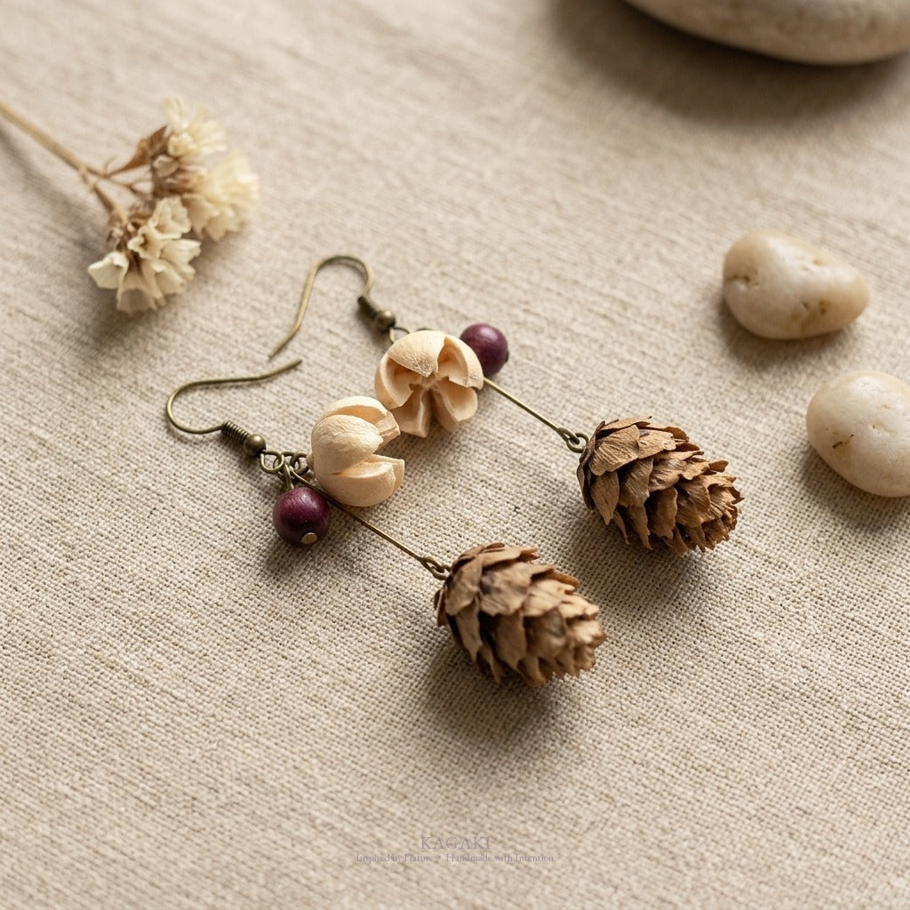 KAGAKI dried-botanical bronze earrings in a soft beige linen still-life with small dried botanicals and pale stones.