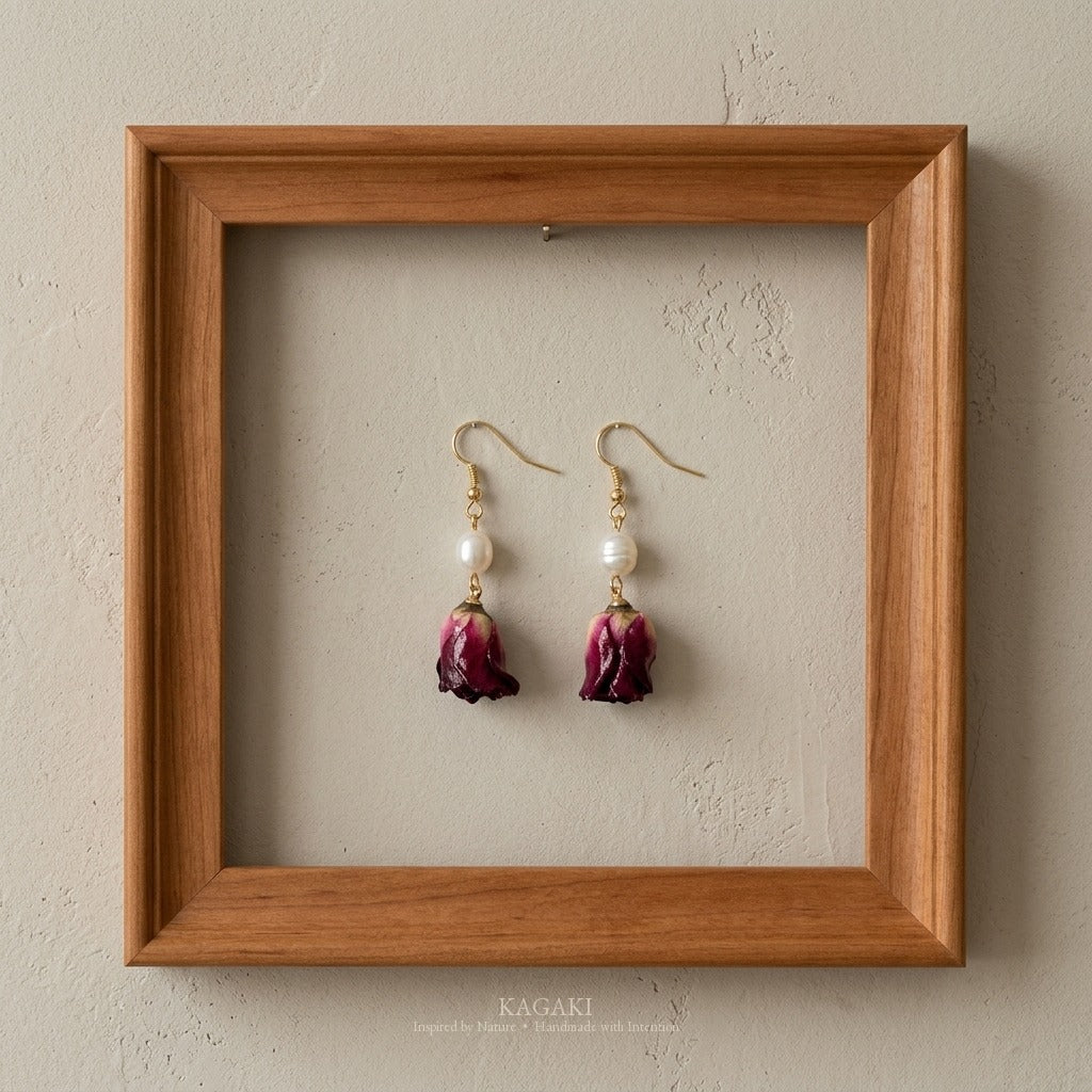 KAGAKI dried rose pearl earrings displayed in cherry wood frame on cream plaster wall, gallery-style botanical jewelry composition