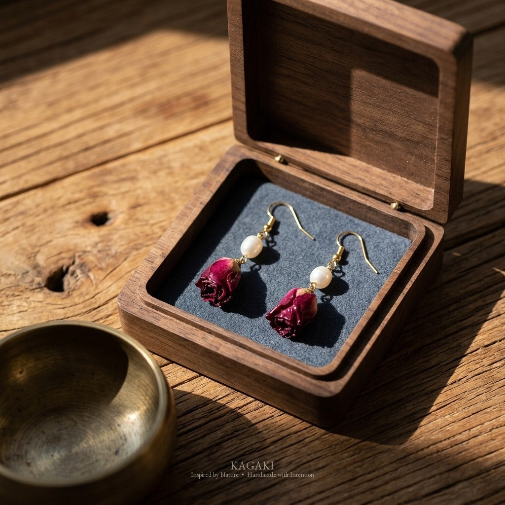 KAGAKI dried rose earring pair laid in dark walnut wooden box with brass bowl on aged wood plank, ritual-object styled composition