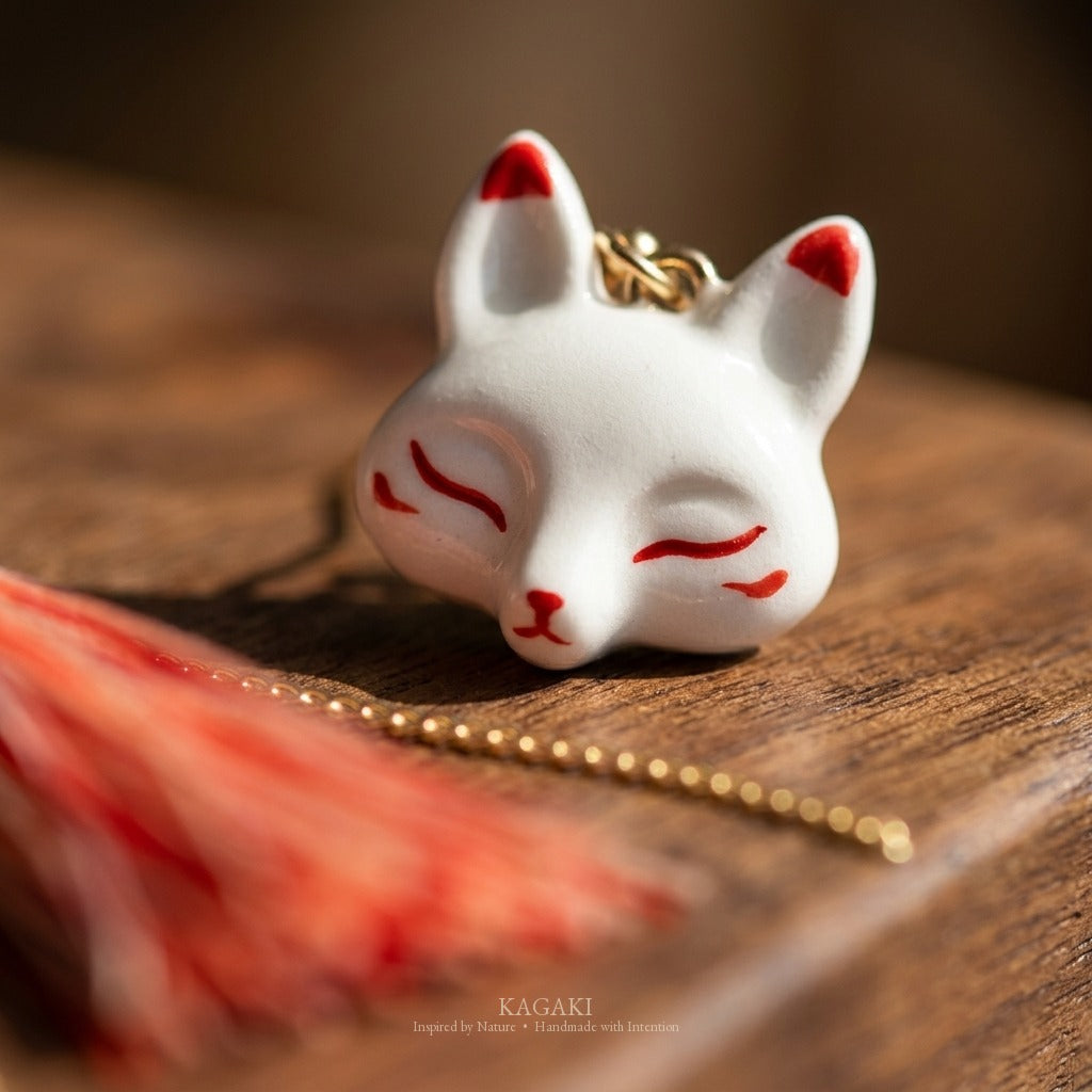 Macro detail of hand-painted red eye and whisker markings on the white porcelain kitsune fox face, showing the small painted craft on the KAGAKI earring