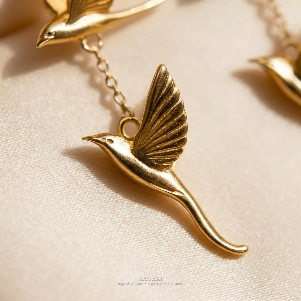 Macro close-up of one KAGAKI gold flying-swallow charm, showing detailed feather etching on the wing.