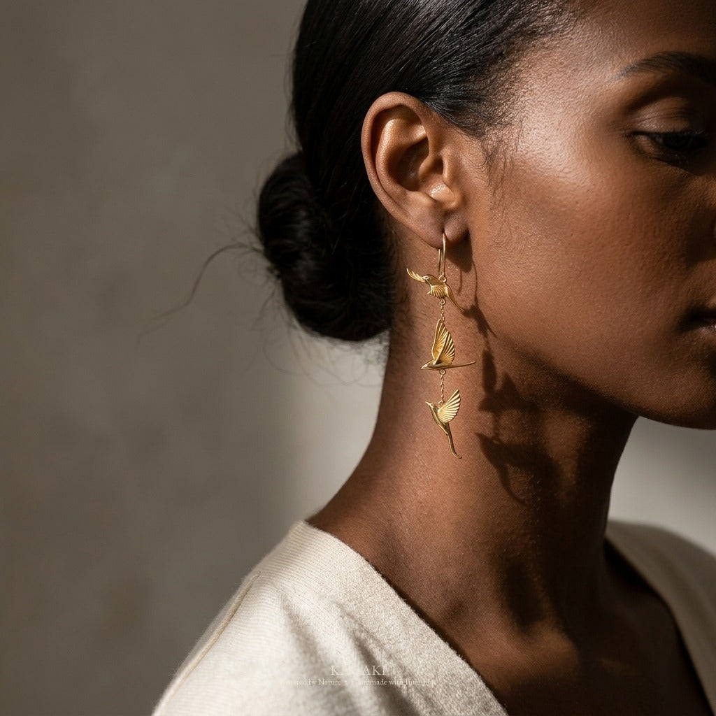 KAGAKI gold flying-swallow earrings worn at the ear, refined fashion-jewelry editorial portrait with directional light and sculptural shadow.
