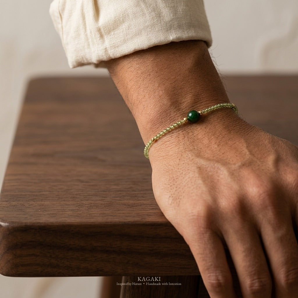 Macro close-up of the KAGAKI green jade bracelet on the wrist, dark green jade focal bead tack-sharp, gold spacers and clasp visible.