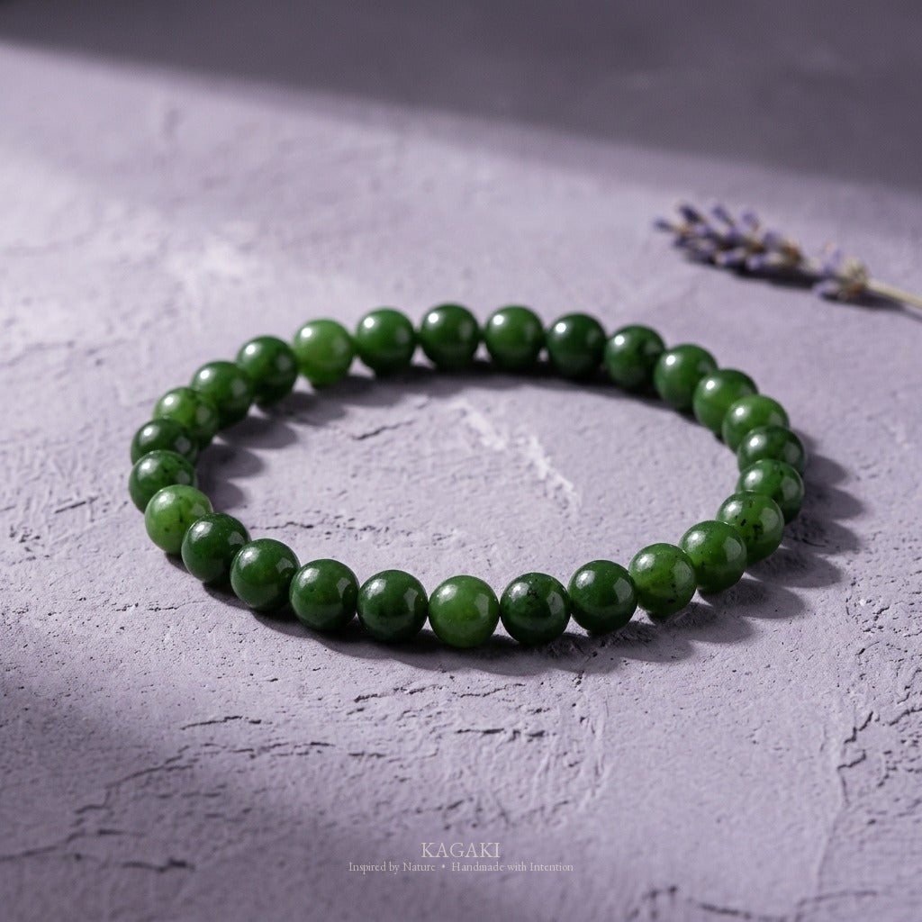 KAGAKI spinach-green jade bracelet styled on weathered lavender-gray plaster with a single dried lavender sprig, raking window daylight.